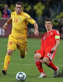 Two white footballers during an international football match between Macedonia and Russia. The footballer in yellow is dribbling past the footballer in red.