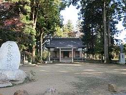 A small Shinto shrine surrounded by trees, with a stone tablet in the foreground
