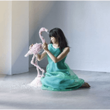 An image of recording artist Haruka Chisuga, sitting down next to a flamingo sculpture.