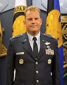 Air Force Brigadier General Jeffrey Cashman in uniform, standing before flags at his promotion ceremony, 2015