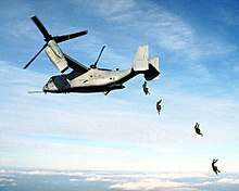 Four U.S. Marine paratroopers jump from the rear loading ramp of an MV-22 Osprey