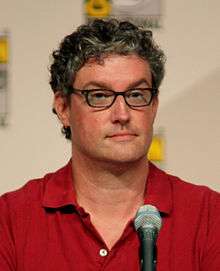 A man with glasses and a red shirt sits in front of a microphone.