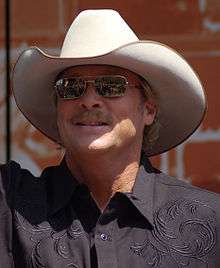 A fair-haired man wearing a white cowboy hat, dark glasses and a black shirt