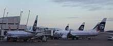 Early morning photo showing Alaska Airlines aircraft parked at an airport terminal, with jet bridges connected to the planes. Five aircraft can be seen in the photo.