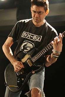 Steve Albini playing guitar, wearing a black t-shirt and ripped blue jeans