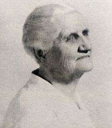 Black and white sideview image of an aging woman with white hair pulled back. She is wearing a white blouse.