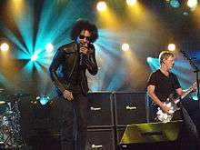 The band Alice in Chains performing on a TV talk show's stage. A male singer, William Duvall, sings into a microphone. A male guitarist plays electric guitar.