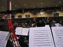 A photo of rock band Alice in Chains in a rehearsal. The photo is taken from inside the orchestra which is playing with the band. Music stands and a bassoon can be seen.