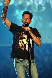 A man wearing a black t-shirt and blue jeans singing into a microphone