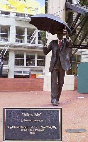 A bronze statue of a man in a business suit; in one hand he is holding an umbrella, while his other arm is extended.