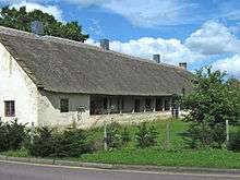 Long single storey building with gray walls and a thatched roof.