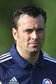 A man with dark hair wearing a dark tracksuit jacket.