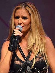 A picture of Andreea Bănică holding a microphone in her hand, wearing a black top.