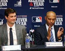 Andrew Miller and Mariano Rivera sit at a table at a press conference dressed in suits.