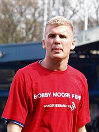 A man with blonde hair who is wearing a red top, which reads "Bobby Moore Fund".
