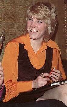 A blonde woman wearing an orange blouse and a black vest