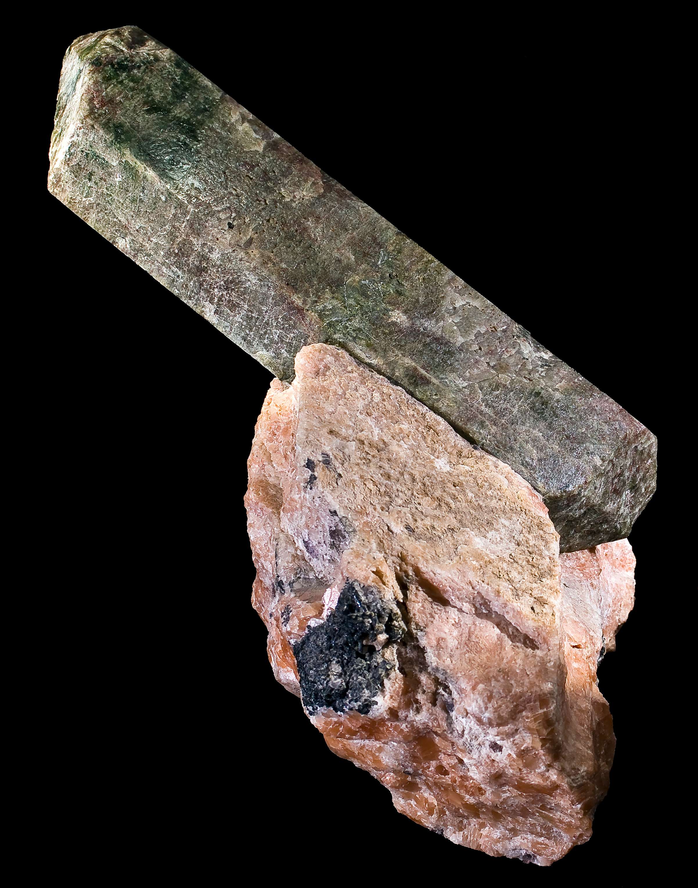 Long prism-like crystal, without luster, at an angle coming out of aggregate-like rock