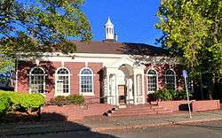Photograph of the Arleta Branch Library, a single-story, brick building with arched windows, wooden entrance portico, and slender cupola