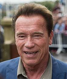 Photograph of the shoulders and head of Arnold Schwarzenegger with a blurry background