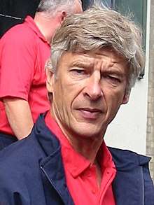 A head-and-shoulders photograph of a gentleman in his 50s. He is wearing a red polo shirt underneath a blue coat, he has grey hair, and his eyes are slightly closed.