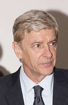 The head and shoulders of a gentleman in his 50s. He is wearing a red polo shirt underneath a blue coat, he has grey hair, and his eyes are slightly closed.