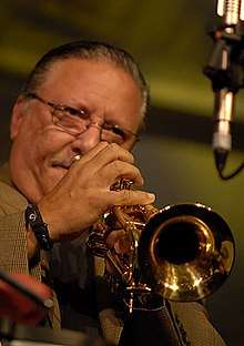 A man with glasses is playing a trumpet in front of the camera.