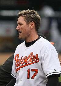A man in a white baseball uniform with the word Orioles on it in cursive orange letters