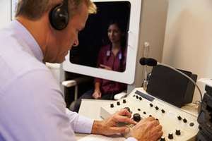 Image showing an audiologist testing the hearing of a patient inside a hearing booth and using an audiometer