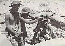 Soldiers loading a mortar tube in a desert position