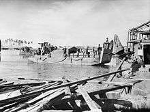 A troop laden landing craft moors in a damaged harbour