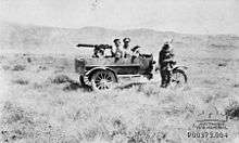 An armoured car showing the driver standing beside the car, passenger sitting in the car with a machine gun and gunner.
