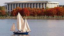 The national library is a rectangular building with tall pillars similar to a Roman/Greek style building. It stands on the shores of a landscaped lake surrounded by deciduous trees with red leaves.