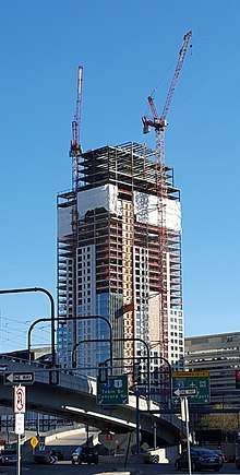  Upward view of a building still under construction with steel members still visible for about the top half of the building and a beige covering on the lower half.