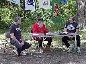 Three middle-aged white men sitting at a camping table outdoors