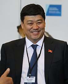 A man in his 40s, attending a large international conference of politicians, smiling.