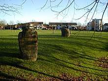 Two standing stones and wooden pilings sitting in a landscaped space surrounded by a modern housing estate