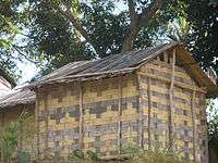 Small, rectangular one-room house with walls and roof made of flattened bamboo