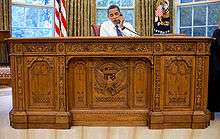 Barack Obama sitting at the ornate Resolute desk in 2009