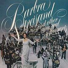 Barbra Streisand appears standing in front of an entire orchestra and other musicians atop a blue background displaying the album's title.