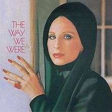 Barbra Streisand appears wearing a black shawl around her head with her hand against a wall.