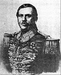 Lithographic half-length portrait of a man with dark hair and mustache who is wearing an elaborately heavily embroidered military tunic bedecked with medals across the chest and heavy epaulets
