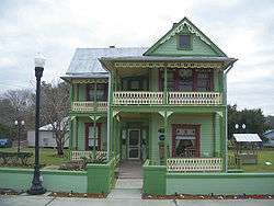 a two-story green house with Victorian ornamentation