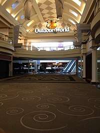 A two-story, carpeted concourse in a largely abandoned shopping mall. Present is a sign reading "Bass Pro Shops Outdoor World".
