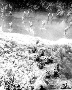 Heavily laden troops wade ashore through heavy surf