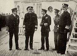 Five men, all in immaculate naval dress, stand on deck.