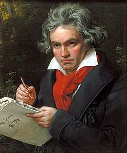 A man with long grey hair holding a pen and music paper
