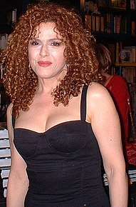 Middle-aged woman with long, curly hair wearing a black sleeveless dress.