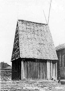 Large wooden rectangular house with steeply peaked roof in thatch