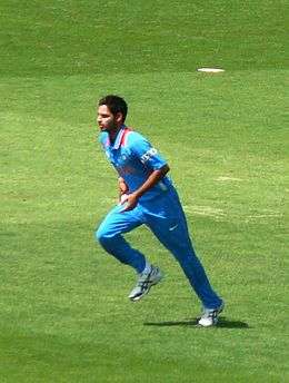A man in a blue Indian jersey and in bowling action.