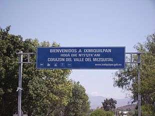 A large overhead road sign says "BIENVENIDOS A IXMIQUILPAN", then (smaller) "HOGÄ EHE NTS'U&#818;TK'ANI", then (larger again) "CORAZON DEL VALLE DEL MEZQUITAL".